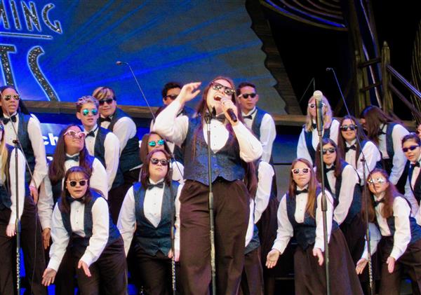 Close up of one high school girl singing a solo, while several other high school singers back her up on stage. Close up of one high school girl singing a solo, while several other high school singers back her up on stage.